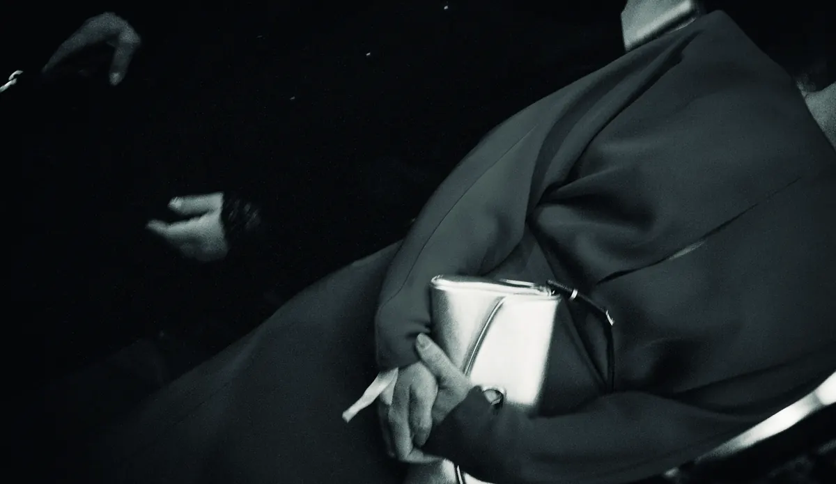 Black and white: a guest in a dark coat holding a silver clutch.